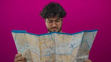 Sakallı ve gözlüklü genç adam canlı pembe bir arka plan üzerinde çalışıyor. Merakı ve keşfi resmediyor..