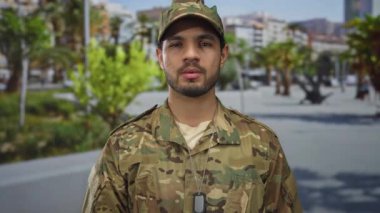 Üzerinde künye olan kamuflaj üniforması giyen İspanyol genç adam şehir sokaklarında duruyor. Onur görevi..