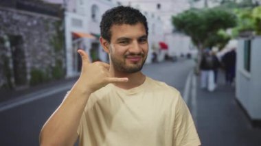Adam meşgul bir şehir caddesinde dururken el hareketi yapıyor ve gülümsüyor; dostça iletişim.