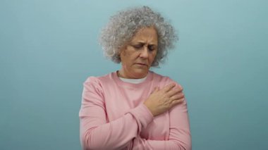 Pembe kazaklı kadın omzunu mavi arka plana yaslıyor. Tarafsız bir ortamda rahatsızlık ve duygu belirtileri gösteriyor..