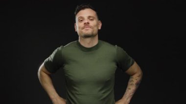 İzole edilmiş, siyah bir arkaplan, dövmeli ve yeşil gömlekli, yakışıklı ve çekici bir tavır sergileyen genç bir adam..