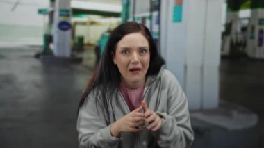 Kadın esmer, gün boyunca açık hava benzin istasyonunda günlük giysiler içinde neşeli ve neşeli bir ifadeyle gülümsüyor..