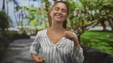 Ağaçların ve çimlerin yanındaki yeşil park yolunda yumruklarını kaldırmış gülümseyen İspanyol genç kadın zafer neşeyi güçlendiriyor..