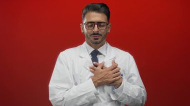 Gözlüklü ve kravatlı genç İspanyol bilim adamı. Parlak kırmızı stüdyoda göğsünü sıkıyor. Tehlike..