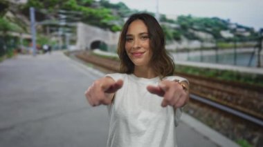 Açık hava tren istasyonunda gülümseyen bir kadın, demiryolunun yanında dikilirken neşeli bir şekilde, yemyeşil ve arka planda bir tüneli olan.