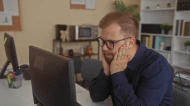 Elleri yanakta olan bir adam binanın içindeki bilgisayar ekranına bakarken gözlük çıkartıyor; stres konsantrasyonu.