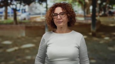 Kadın parkta, açık arka planda esmer kıvırcık saçlı gözlük takarak güneşli bir günde düşünceli bir anı işaret ediyor..