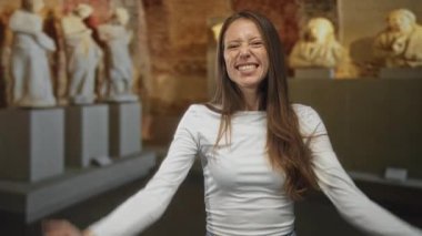 Bir sanat galerisinde sıkılmış yumruklarını kaldıran genç İspanyol kadın, gözleri kapalı gülümsüyor ve kolları zaferle kaldırılıyor; sevinç zaferi.