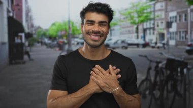 Sandık tutan ve park halindeki bisikletlerin ve bulanık binaların önünde gülümseyen Latin asıllı genç adam..