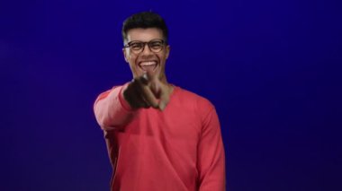 Gözlüklü genç adam kameraya bakarken gülümsüyor.