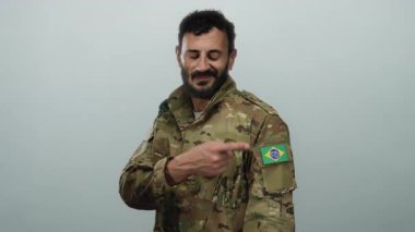 Askeri üniformalı İspanyol adam kolunda Brezilya bayrağı olduğunu gösteriyor. Gri bir arkaplanda gururlu bir ifade ve sakalla duruyor..