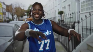 Mavi basketbol forması ve beyaz bileklikle elleri sokakta kalp oluşturan adam; Joy Love Community.