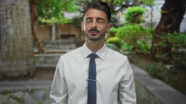 Beyaz gömlekli bir adam işaret parmağını yukarı kaldırıyor ve orman düzeninde gökyüzüne bakıyor..