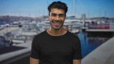 Siyah tişörtlü bronzlaşmış adam, güneşli iskele rıhtımında sessizlik için parmaklarını dudaklarına tutar; gizlilik gizlilik huzuru.