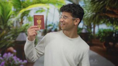 Ormanda elinde pasaport tutan genç İspanyol adam kameraya gülümsüyor, heyecanlı seyahat tutkusu..