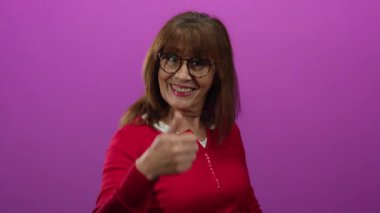 Hispanik son sınıf öğrencisi, kırmızıyla gülümseyen ve pembe arka plana karşı olumlu bir jest yapan bir kadın..