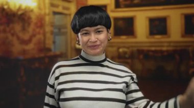 Süslü süveteri içinde utangaç bir şekilde gülümseyen bir kadın kapalı alanda kültürel keşiflerin samimi bir anını yakalıyor..