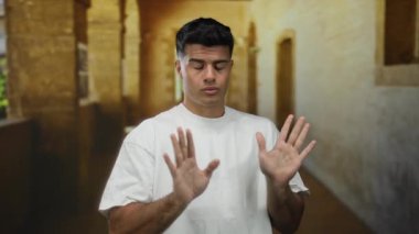 Elleri havada genç bir adam eski bir üniversite koridorunda duruyor, sakin ve odaklanmış, tarihi taş mimarisine karşı koyuyor..