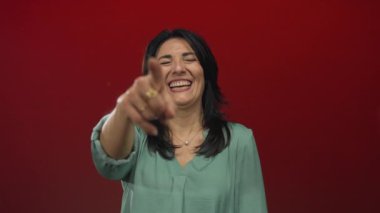 Stüdyoda gülümseyen ve kamerayı işaret eden orta yaşlı İspanyol kadın, neşe ve kahkaha.