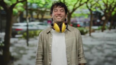 Ses geçirmez kulaklık takan İspanyol bir adam ağaçlarla kaplı canlı bir sokağa el uzatıyor. Kamerayla uğraşırken kendine güven ve cazibe yayıyor..