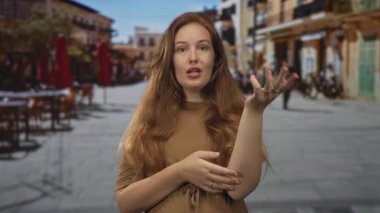 Cafe masalarında kırmızı şemsiyeli, güneşli bir yaya caddesinde el çırpan bir kadın..