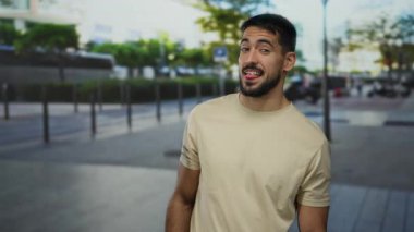 Sokak sahnesinde şakacı bir şekilde dil çıkaran genç adam, gündüz vakti şehir ortamında rahat bir kıyafetle mutlu bir ruh hali sergiliyor, eğlence ve modayı zahmetsizce harmanlıyor..