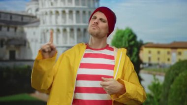 Sarı ceketli ve kırmızı bereli genç adam sidik kulesine karşı hareketler yapıyor..