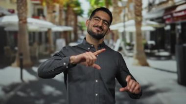 Sokak ortasında duran genç bir adam elleriyle bir kalp oluşturuyor ve çekici bir şekilde gülümsüyor..
