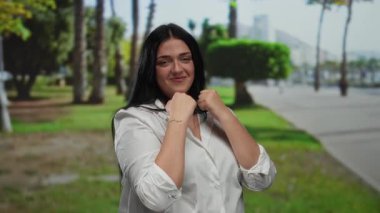 Parkta açık havada boks yapan, yemyeşil bir kadın, gün ışığında sakin bir ortamda kendine güven ve güç gösterisi yapıyor..