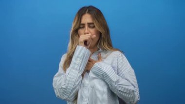 Genç sarışın kadın ağzını yumruk ve göğüs debriyajı ile kapatıyor mavi stüdyoda yakın plan portrede; rahatsızlık verici hastalık.