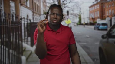 Sokakta görünür elle parmaklarını çimdikleyen adam, kırmızı polo 'da ileri doğru şaşı bakışlar; şüphecilik küçük vurgu.