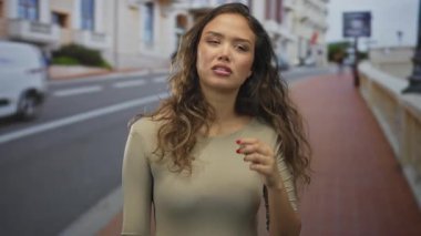 Şehir caddesinde yürüyen kadın düşünceli görünüyor, binaların arka planına ve kırmızı tuğlalı kaldırıma karşı kurulmuş, sakin bir açık hava ortamı sergiliyor..