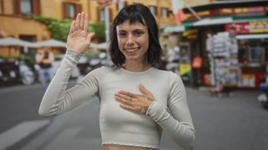 Genç kadın el kaldırıyor ve el ele tutuşuyor. Dükkanlar ve scooterlarla dolu bir caddede. İçtenlikle güven..