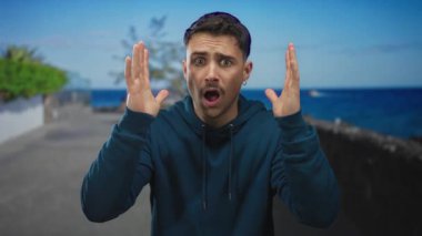 Genç İspanyol bir adam arka planda berrak mavi deniz ile bir deniz gezinti şaşırmış görünüyor, canlı bir ifade ve sakin bir sahne sergiliyor.