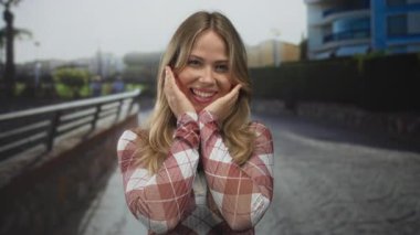 Sarışın, beyaz kadın bardakları sokakta gülümserken elleri ile yanakları; sevinç sürprizi sevinç neşesi.