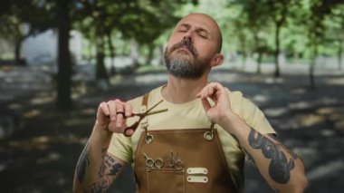 Açık havada güneşli bir parkta duran, önlük giyen ve elinde makasla yeşil bir yüzle dolaşan bir adam..