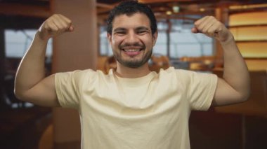 Adam bir restoranda beyaz tişört giyerek kollarını esnetiyor; kendine güven duygusu pozitiflik motivasyonu.