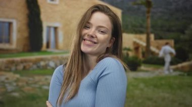 Genç bir kadın kollarına sarılıyor ve sıcak sabah güneşi altında taş bina girişinde gülümsüyor. Huzur..