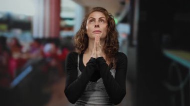 Restoran terasında dikkatlice namaz kılan bir kadın. Arka planı bulanık. Şehir merkezinin altında açık bir kafe var..