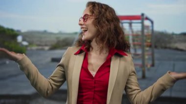 Açık havada gülümseyen kırmızı gözlüklü ve bej ceketli bir kadın oyun parkında arka planda bulanık bir şekilde eğlenmeyi ve eğlenmeyi öneriyor..