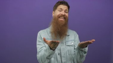 Sakallı ve kot ceketli bir adam mor bir stüdyoda avuçlarını açık tutuyor içerik için yer sunuyor; keyif daveti.