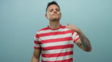 İspanyol erkek dikkatle uzaklığa bakıyor, saf mavi bir arka plana karşı duruyor, dövmelerini ve kendinden emin duruşu olan günlük çizgili gömleğini vurguluyor..