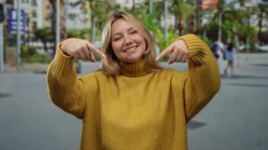 Sarı süveter giymiş, arka planda bulanıklık olan şehir caddesini işaret eden, neşeli şehir yaşam tarzını somutlaştıran açık hava manzaralı bir kadın..