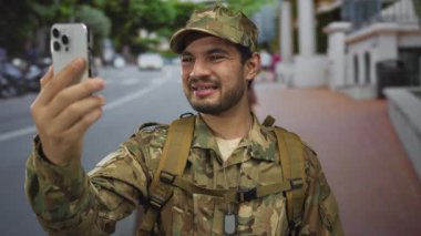 Kamuflaj üniformalı bir adam, gündüz vakti sokakta akıllı telefonu kol mesafesinde tutuyor. Gurur görevi vatanseverlik yoldaşlığı..