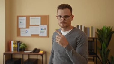 Ofisteki genç adam, düzenli bir çalışma alanında profesyonel ama rahat bir atmosfer yaratan tablolar ve kitaplarla çevrili gündelik kıyafetlerle güvenle gülümsüyor..