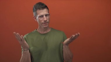 Avuç içi açık el hareketi yapan ve stüdyoda portakal arka planına karşı elini kaldıran adam, düşünceli bir yansıma..