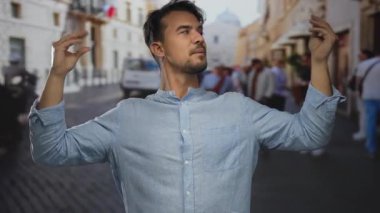 Canlı bir şehir caddesinde, arka planda bulanık yayalar ve tarihi binalar olan neşeli bir konuşmayı taklit eden İspanyol genç adam..