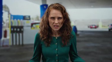 Benzin istasyonunda el kol hareketi yapan bir kadın arka planda bulanık yakıt pompalarıyla açık havada duygularını ve gündelik tarzını sergiliyor..