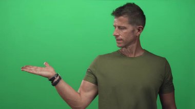 Avuç içi açık bir adam yeşil stüdyoda, omuz silkiyor ve her iki tarafı karşılaştırıyor; şüphe tefekkür.