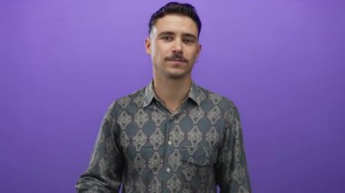 Şablonlu tişörtlü genç İspanyol bir adam, düşünceli bir şekilde kafasını soyutlanmış bir mor arka plana sürtüyor, tefekkür ve iç gözlem yapıyor..